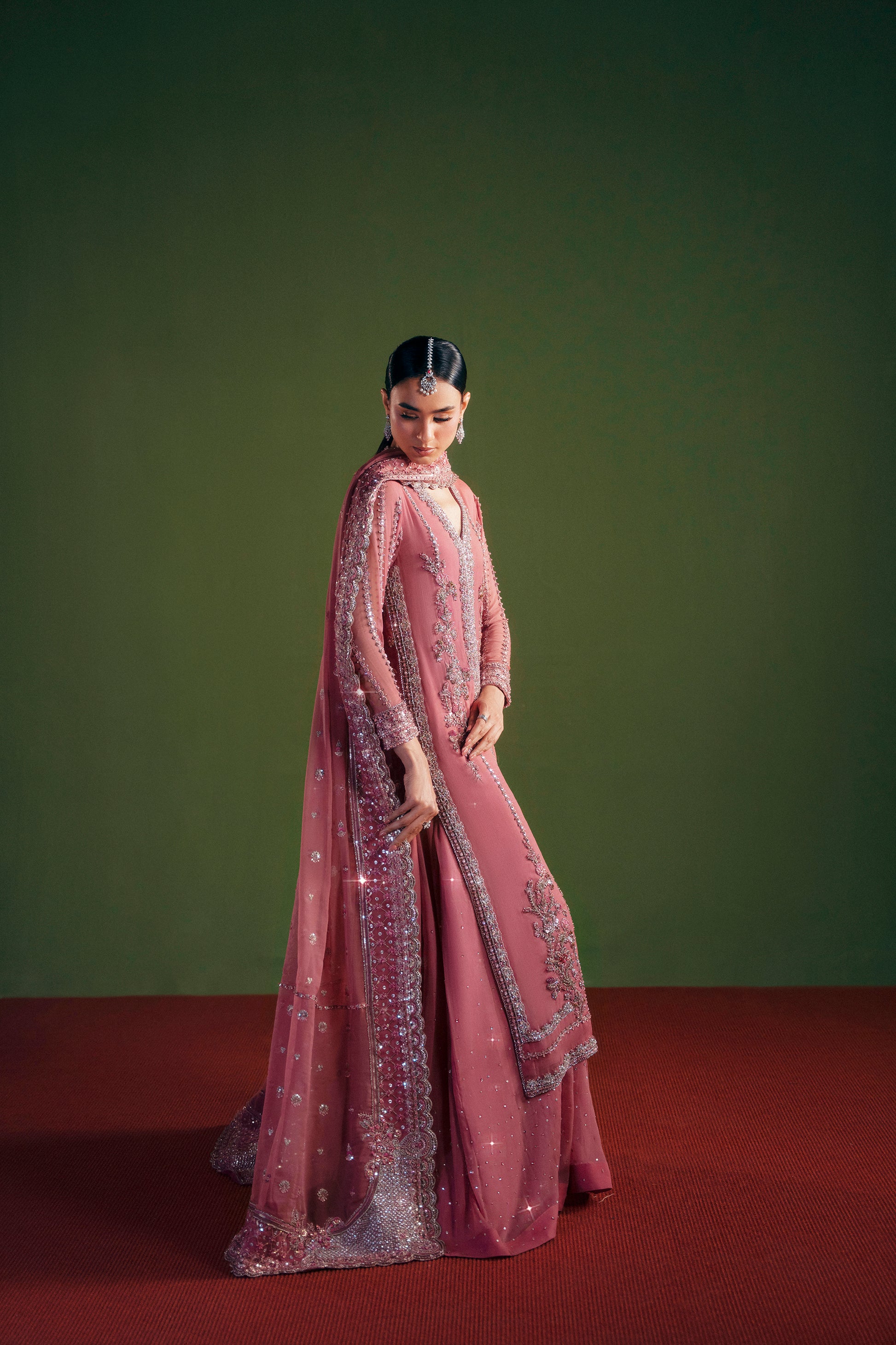 Woman in a pink traditional outfit with intricate designs against a green background|designer women’s clothing embroidered long shirt detail