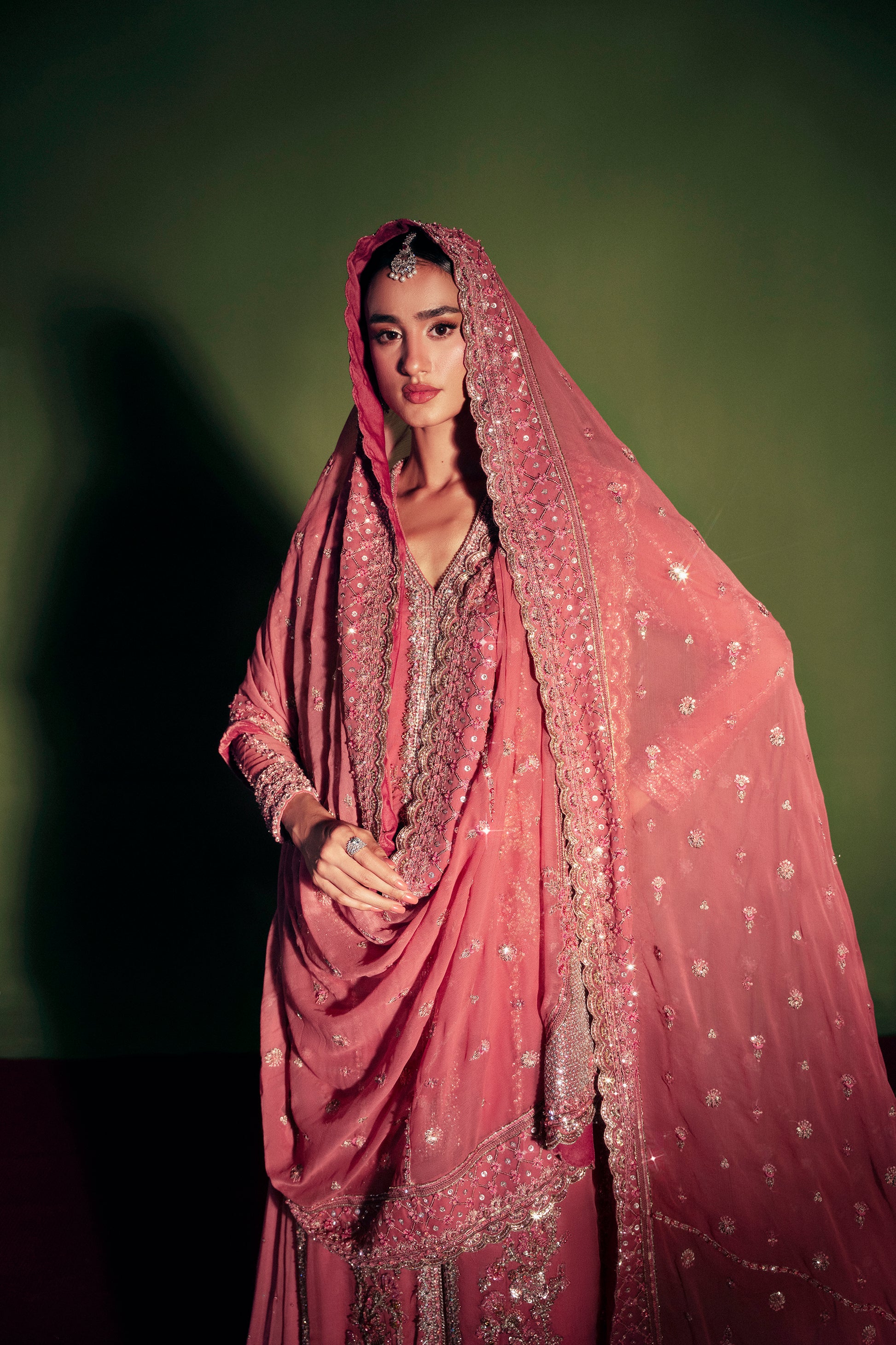 Woman wearing a pink saree with a matching veil against a green background|premium women’s fashion outfit with crystals and pearls