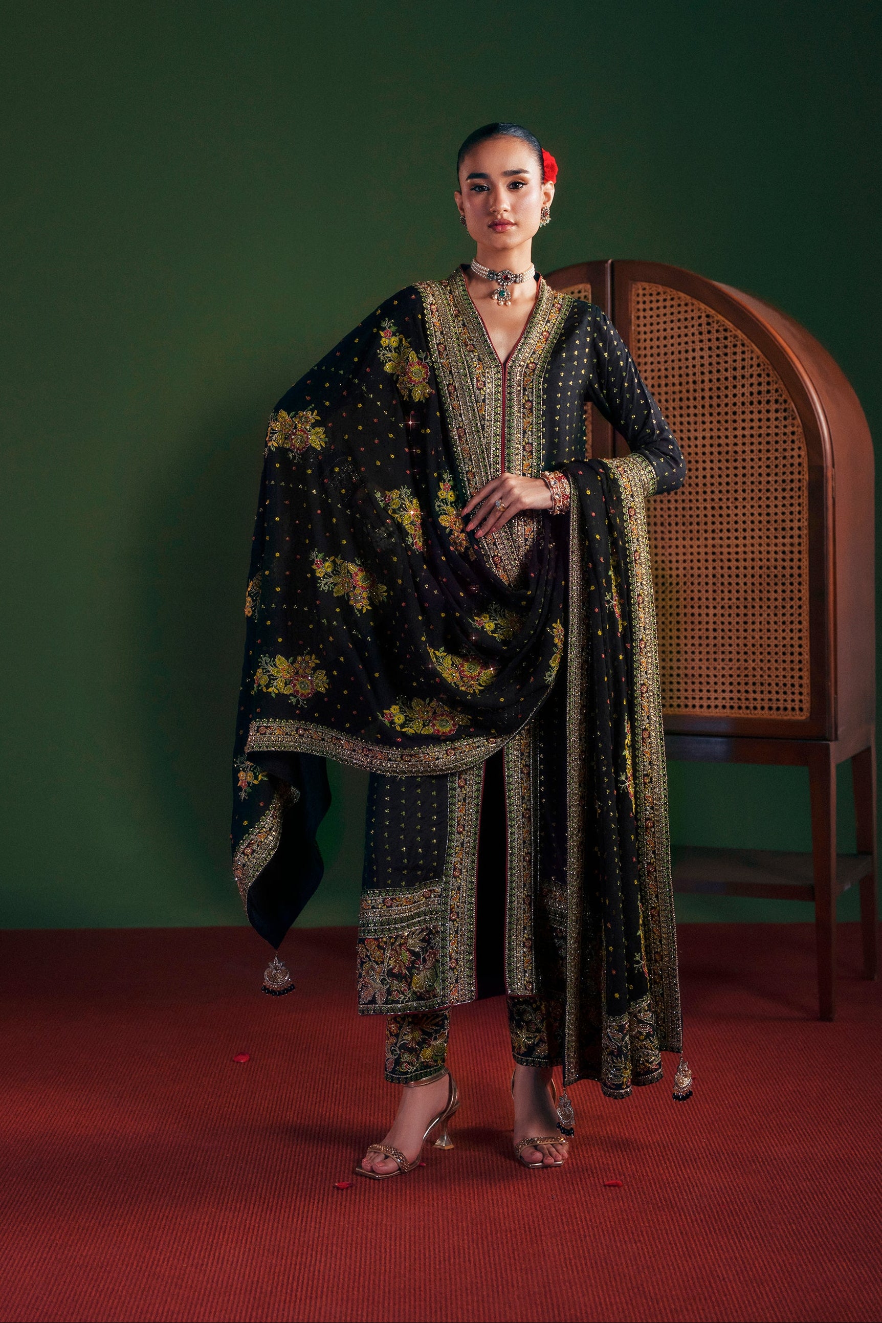 Woman in traditional outfit standing against a green wall with a wooden chair|Midnight Blooms long shirt 3 piece luxury silk outfit