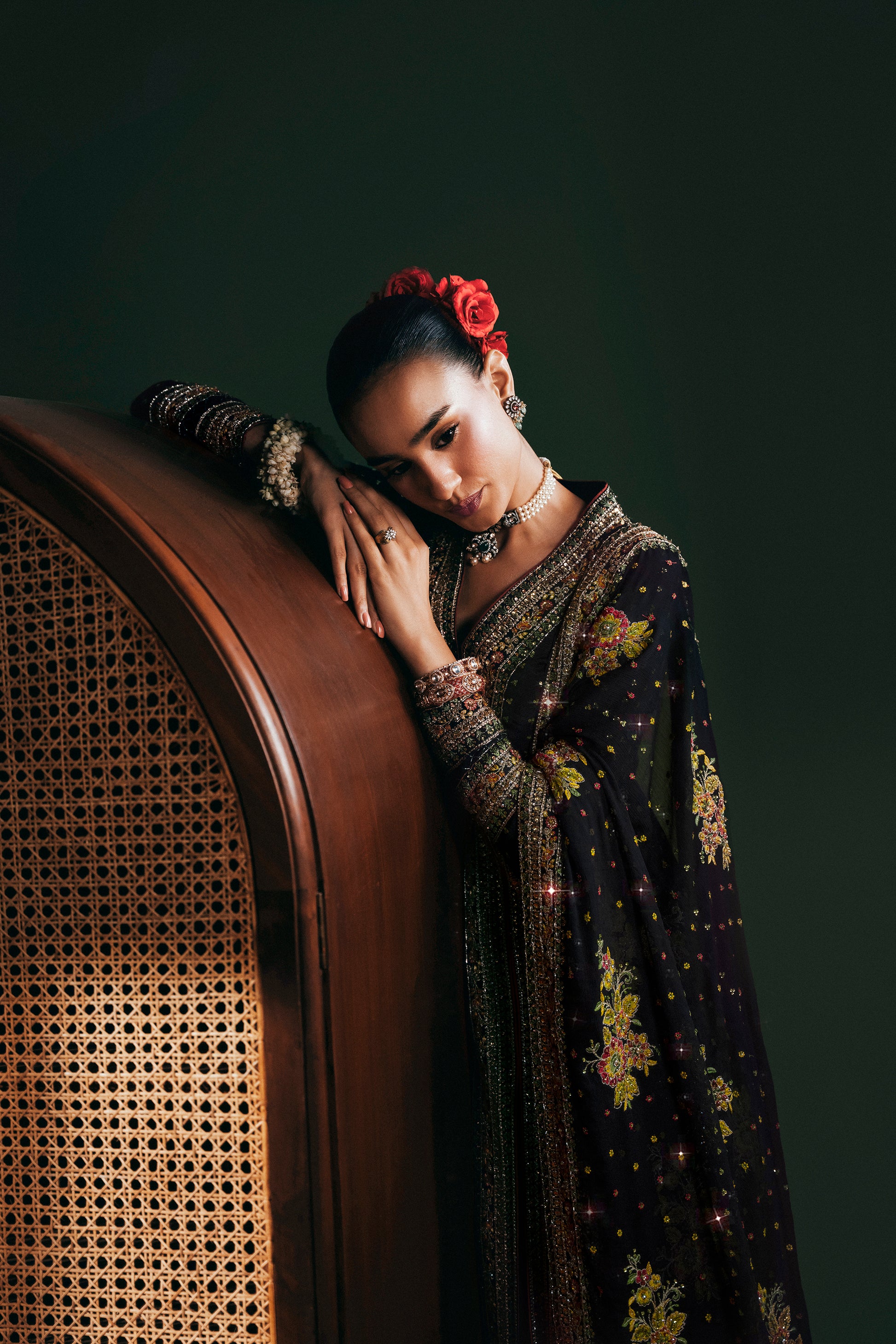 Woman in a floral dress leaning against a vintage chair with a dark background|Model wearing Midnight Blooms luxury ensemble formal outfit